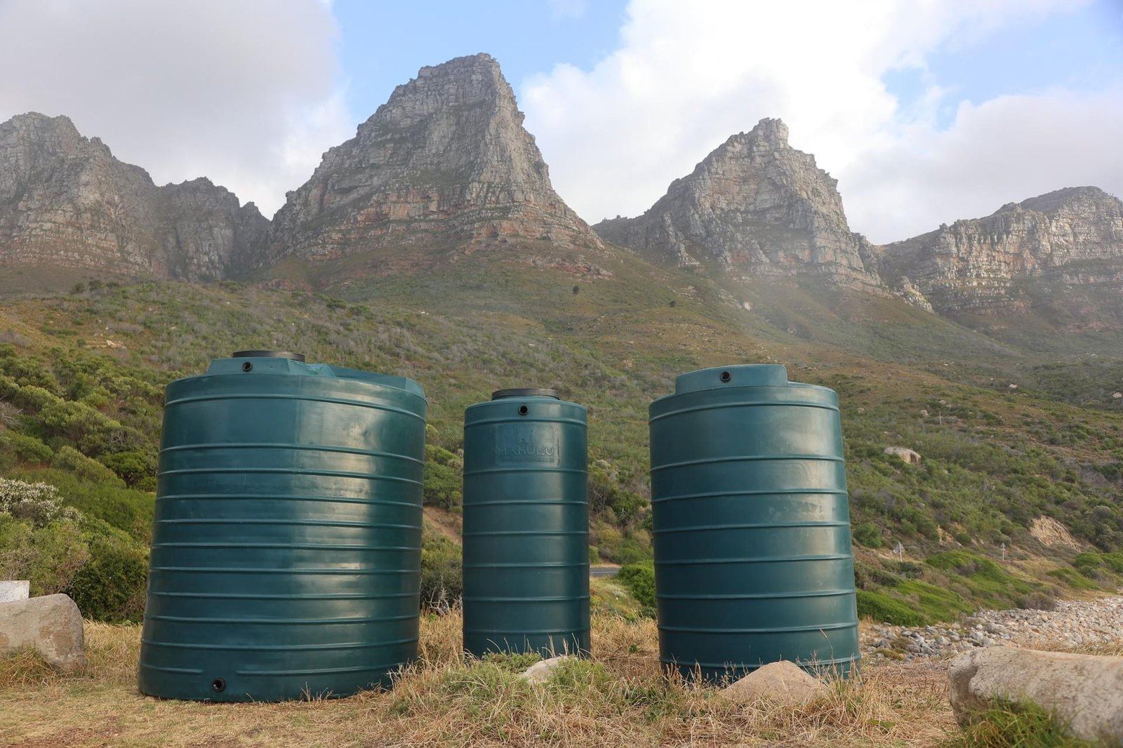 Three Emerald Green Makulu water tanks standing on fynbos with mountains behind